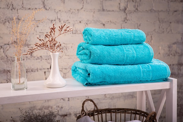 Rack with a stack of three color turquoise towels and baskets with clean white towels and toilet decor near brick wall. 