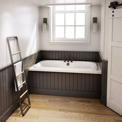 A  large tub in a bathroom recess with gray paneling along the tub base and surrounding walls. 